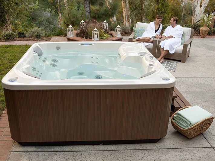 A Hot Spring spa with low-maintenance features is depicted in the foreground, inviting you to unwind while a couple enjoys its benefits in the background.