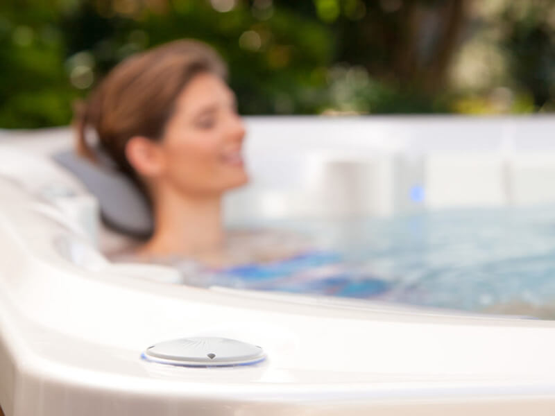 Close-up of a built-in hot tub speaker, with a blurred background of a woman relaxing in the warm, bubbling water.