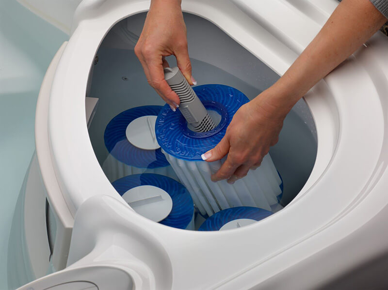Close-up of a person replacing a blue and white hot tub filter, demonstrating maintenance of the filtration system for clean and clear water.